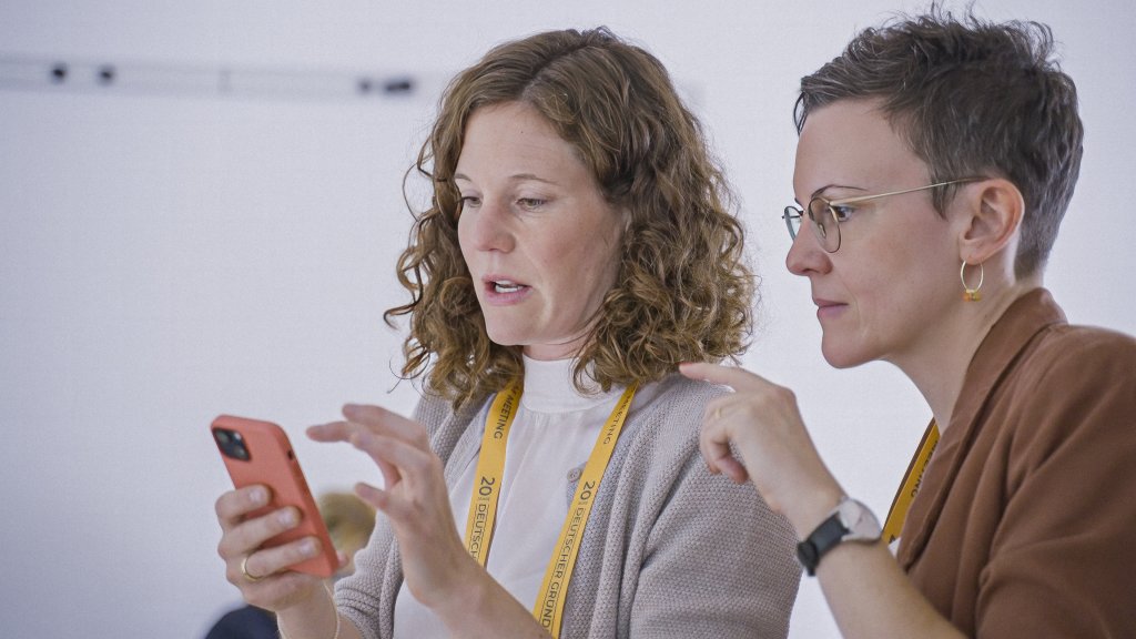 Zwei Frauen schauen auf ein Handy. Innovative Tools für Ihre weltweite Belegschaft.